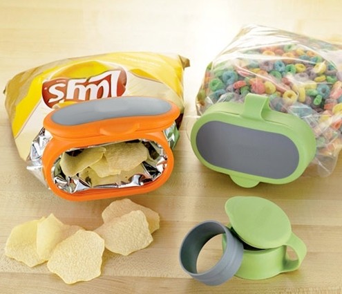 Opened Lays pack sealed with orange and grey colored cap, cereal pack sealed with green and grey colored cap, some potato chips and a green and grey colored cap placed on a wooden tabletop