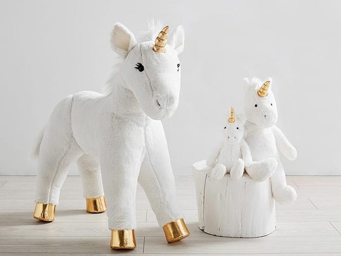 Three gold horned and gold hooved white stuffed toys of unicorns on a white floor and a white background