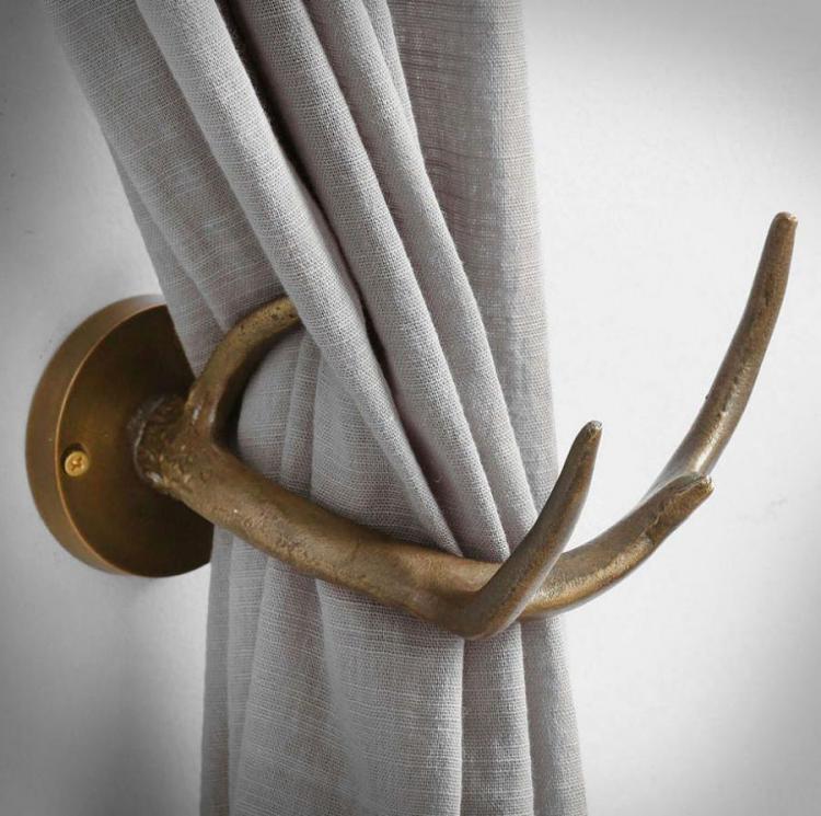 White cotton curtain held by a metal tieback antler