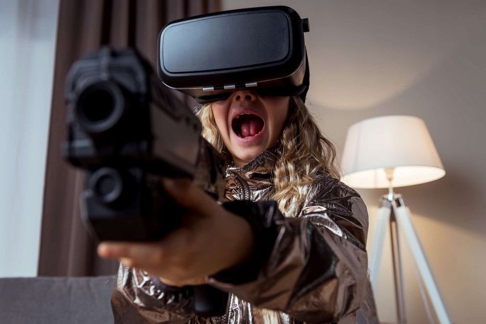 A young girl wearing VR and is getting violent while holding a toy gun