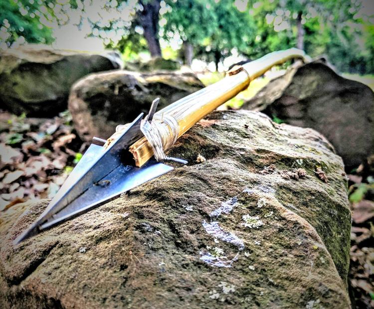 Assembled stainless steel Credit Card Survival Spear set on a rock in the forest