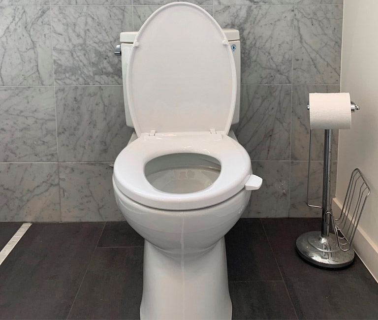 White-colored antimicrobial toilet seat handle on a white commode on a black floor