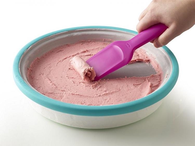 Strawberry flavored icecream rolls in an instant ice cream maker with a hand holding purple-colored spatula
