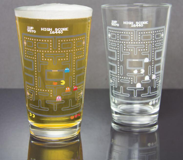 Two pac man pint printed glasses; one with colored liquid and one is empty on grey surface