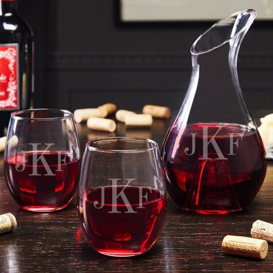Wine-filled wine decanter and wine-filled glasses with some corks and a wine bottle on dark brown wooden surface