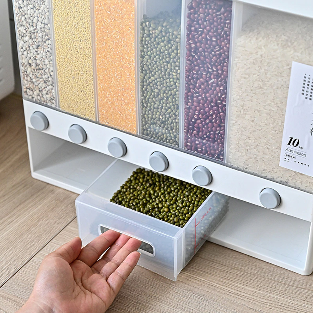 Transparent wall mounted food dispenser filled with multi-colored pulses and rice with a transparent bowl filled with green pulses