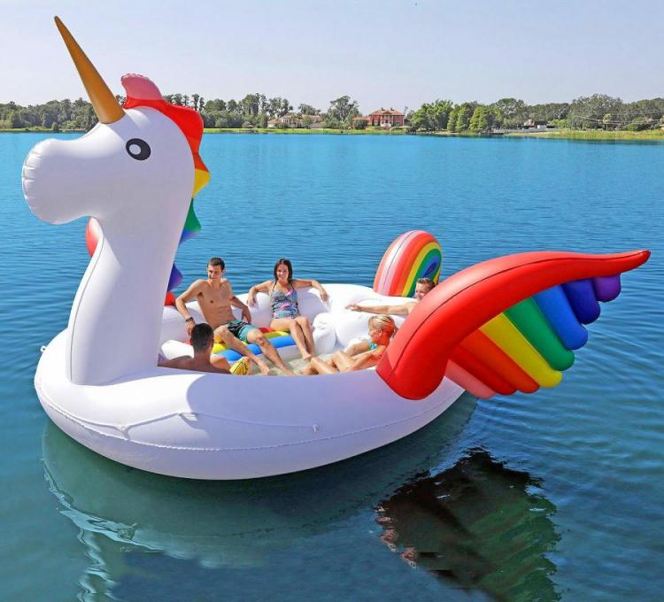 Four persons sitting in a giant white and rainbow-colored unicorn pool float