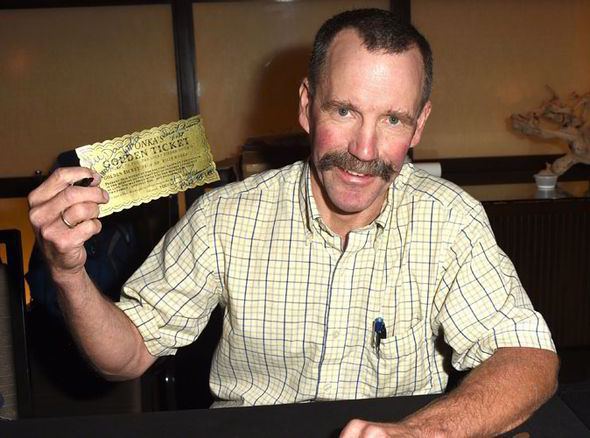 Peter Ostrum wearing a yellow polo shirt and holding a famous golden ticket from the movie Willy Wonka & the Chocolate Factory 