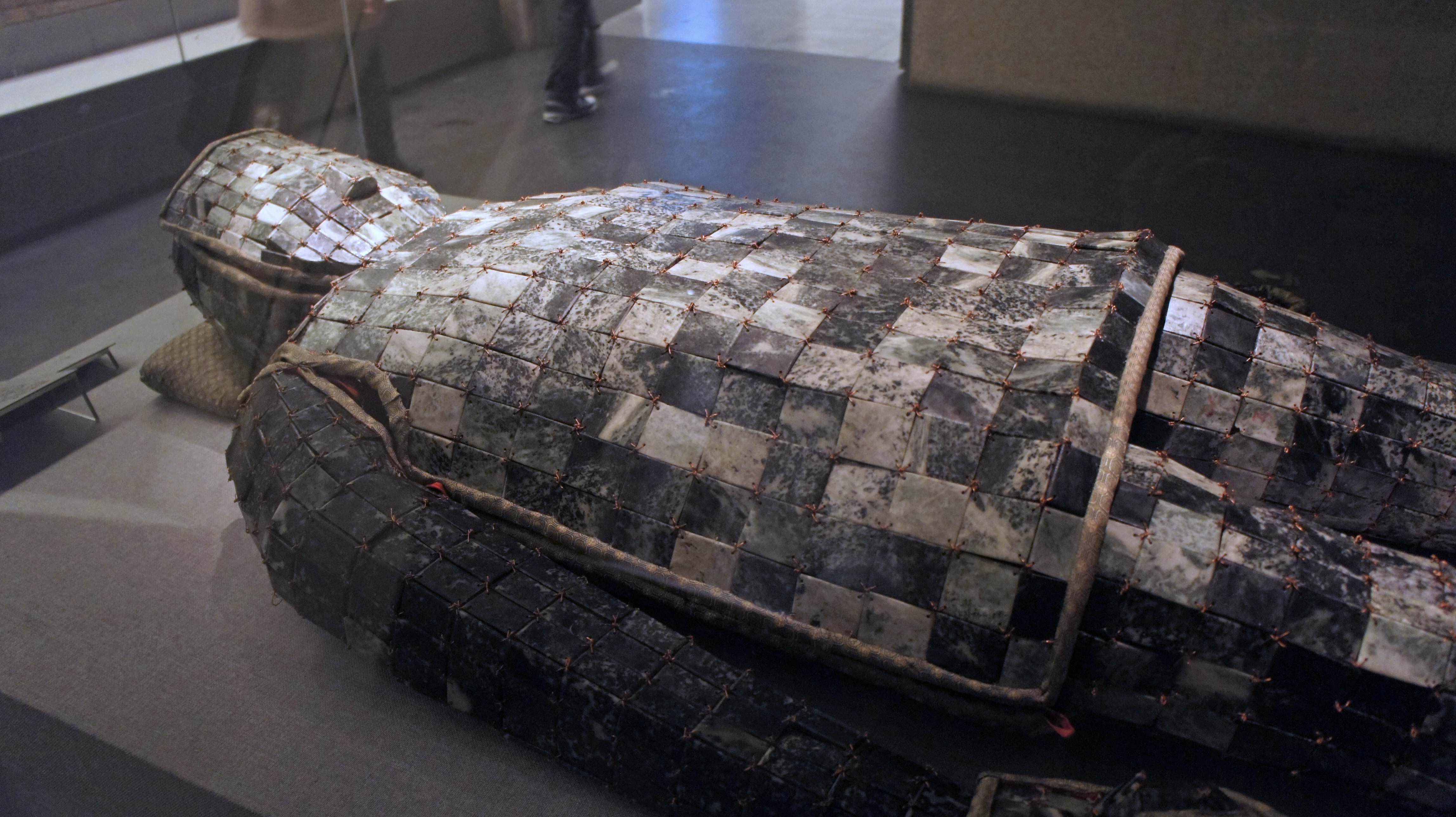 An angular shot of brown and skin-colored metal jade burial suit on a grey surface