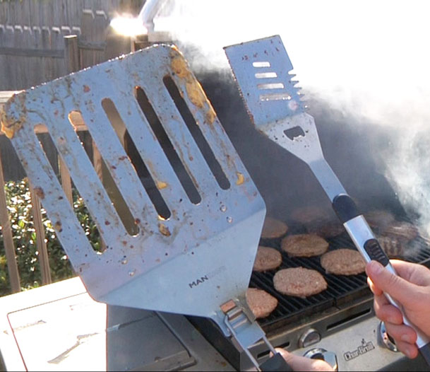 A man holding a giant steel grilling spatula and an normal size grilling spatula in his other hand