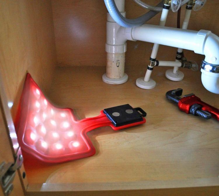 A red-colored flexible flashlight sheet placed in a wooden cabinet near a wrench and white pipes