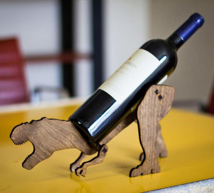 A brown wooden t-rex shaped wine bottle holder on a yellow surface 