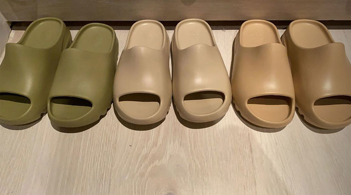 Green, skin, and skin-brown Yeezy slippers on a skin-brown wooden floor