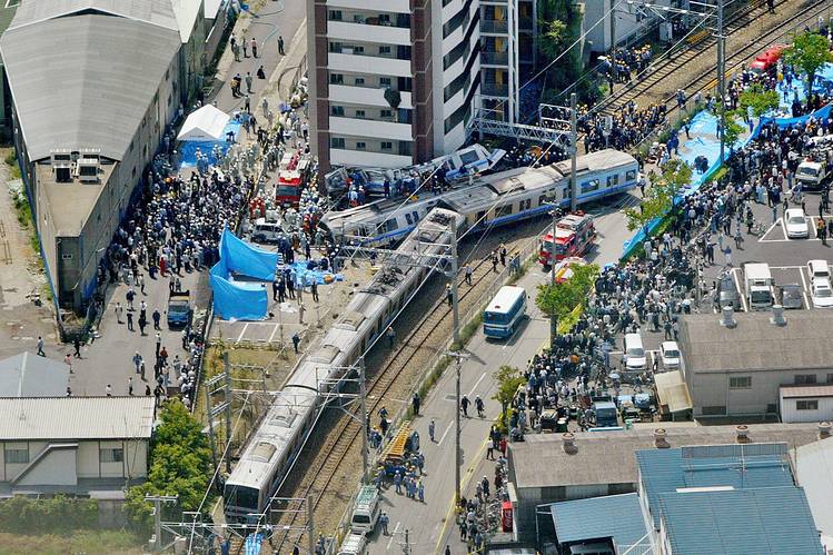 A high-speed west japan railway train comes off its rails with many people surrounds it