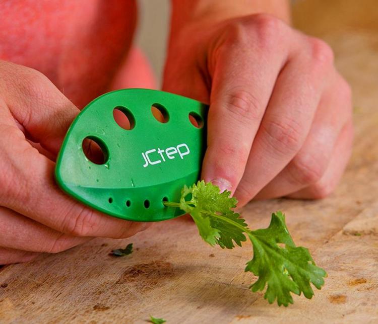 A green-colored herb stripper tool removing stems from coriander