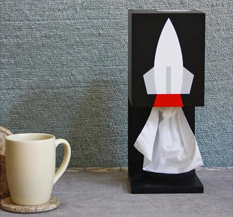 White and red rocket on a black box on a grey surface