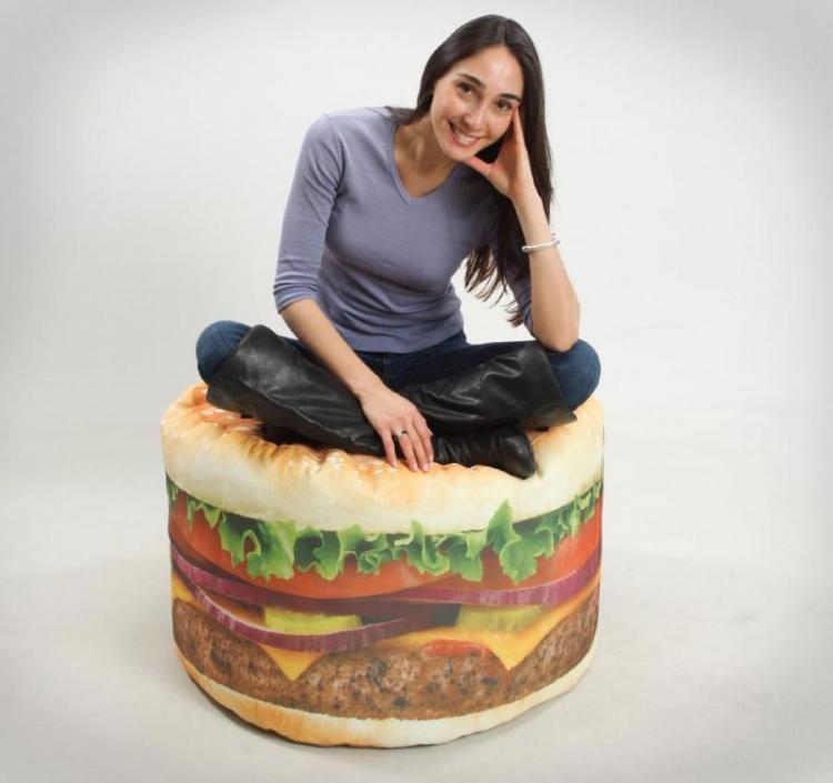A grey shirt and jeans wearing girl sitting on acheeseburger cushion