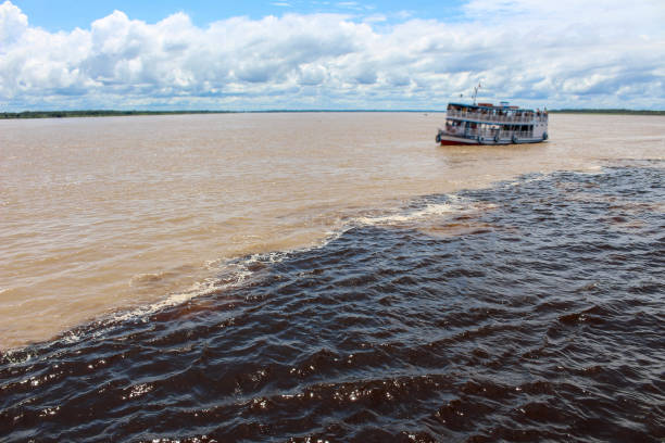 Brown colored Amazon River meets the blue colored Tapajós River and a boat on the brown-colored amazon river