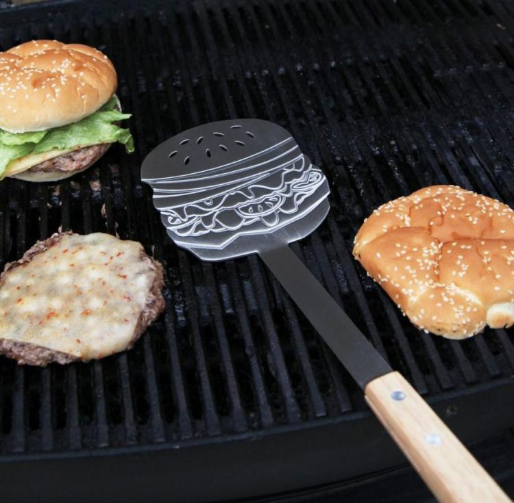 Cheeseburgers grilling on a black coal grill and a wooden cheeseburger shaped spoon on the grill