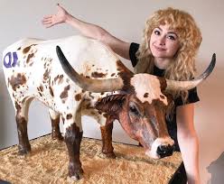 Natalie sideserf standing next to a hyper-realistic white and brown colored cow cake