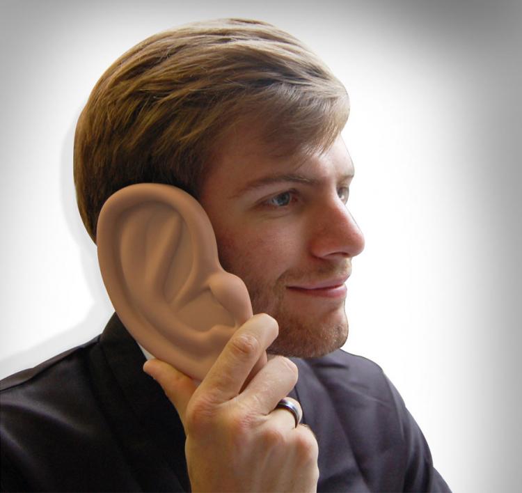 Giant skin-colored ear phone case held by a blue shirt man