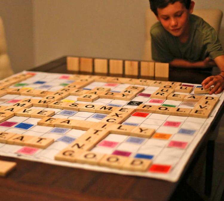 A green shirt wearing boy playing wooden blocks word scramble game on a dark brown wooden table