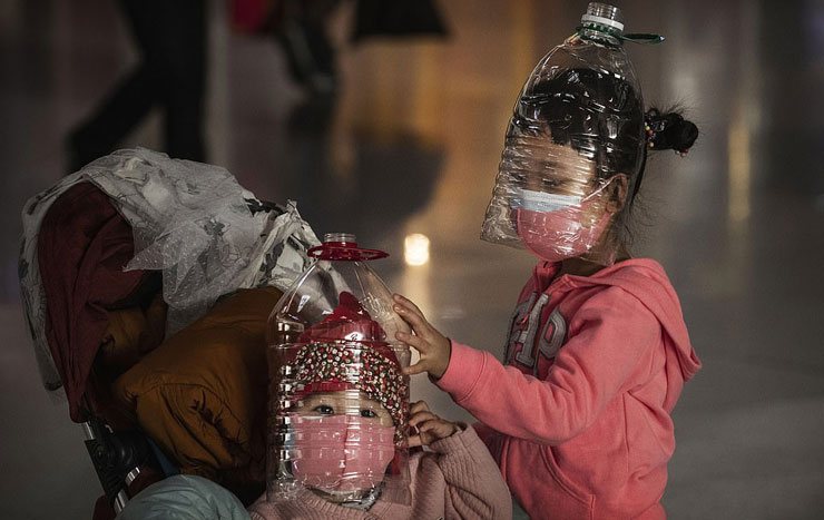 A young girl and a toddler wearing a double layer facemask also covered with a plastic container