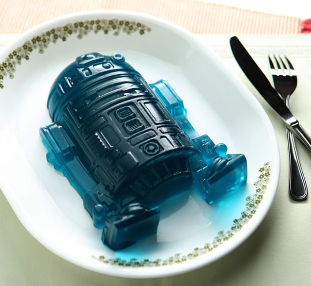 The blue colored robotic ice cube on a white plated beside a fork and a knife on a wooden table