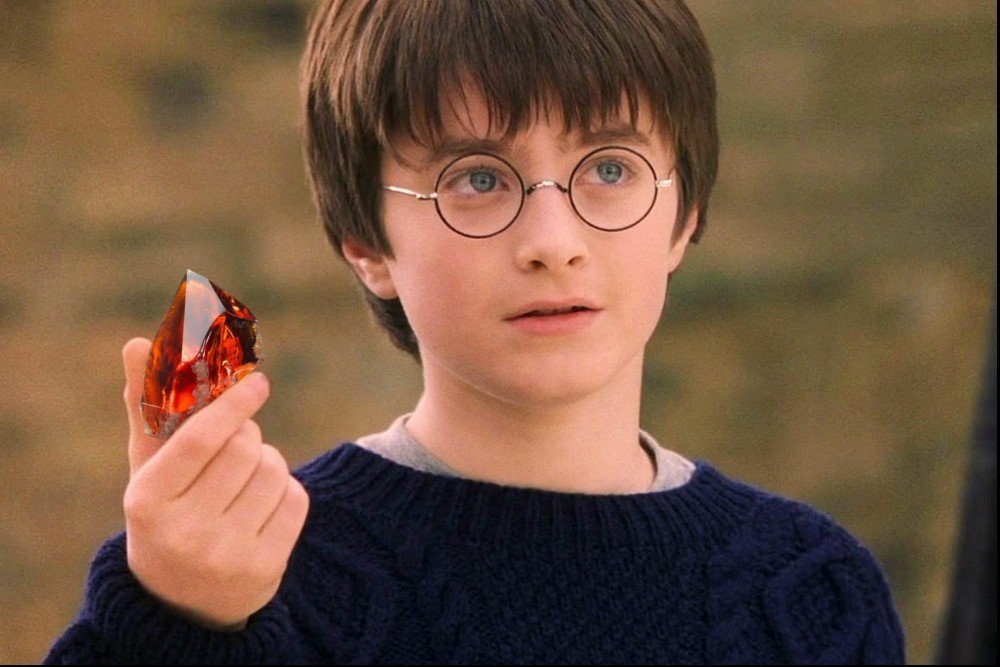 Harry potter wearing a blue sweater and holding a red stone