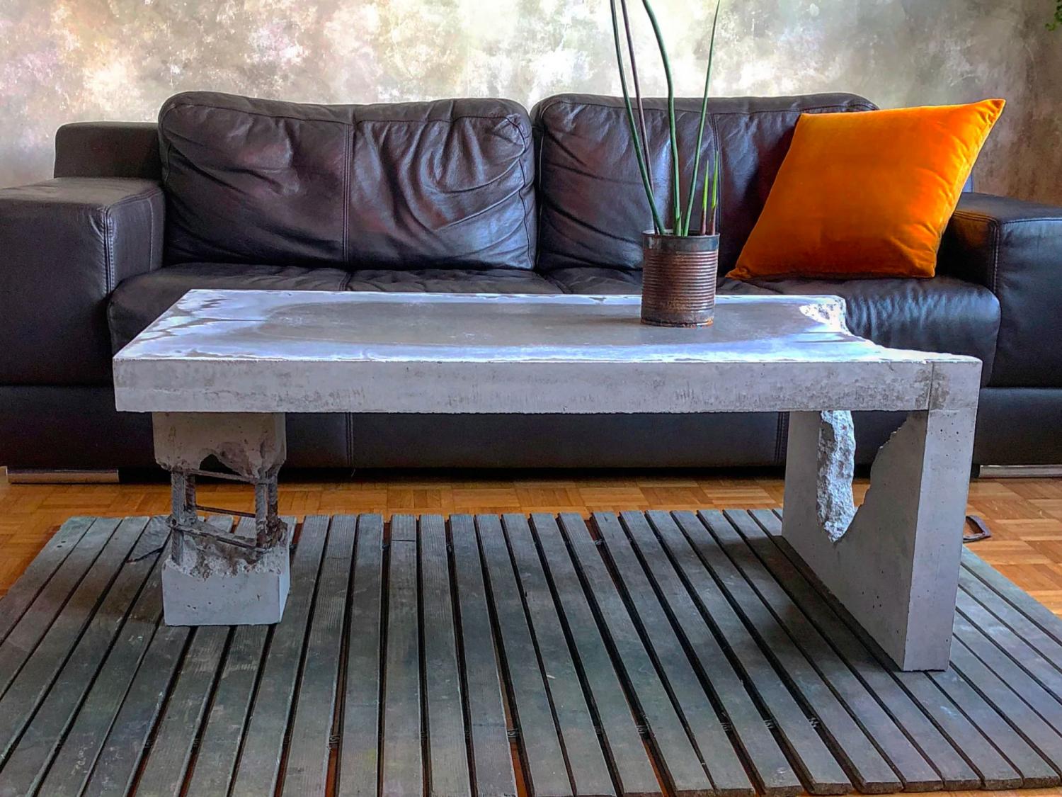 Concrete coffee table besides a black leather sofa on a grey striped software