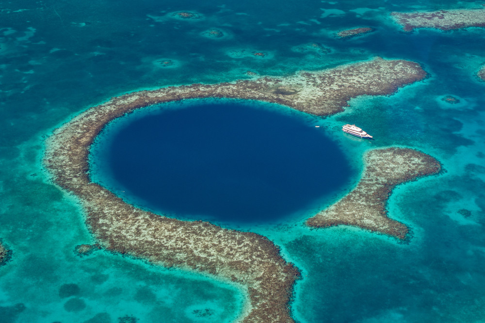 A white-colored ship in the blue and dark blue colored Great blue hole of Belize