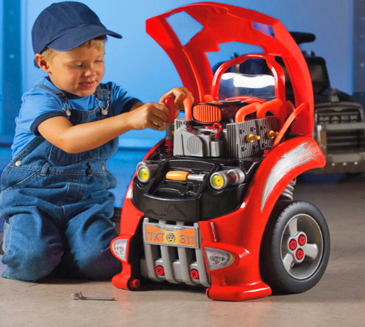 Blue shirt and a blue cap-wearing boy repairing his red and black mini car in the garage