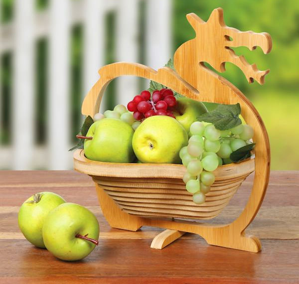 Wooden dinosaur basket containing green apples, yellow apple, red and green grapes on dark brown wooden table