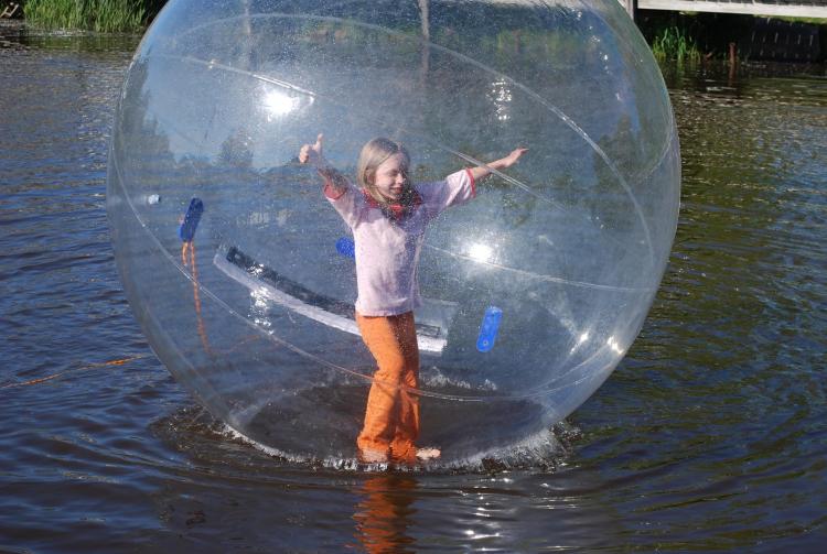 A girl wearing white shirt and orange pants in inside a giant transparent water ball in a lake