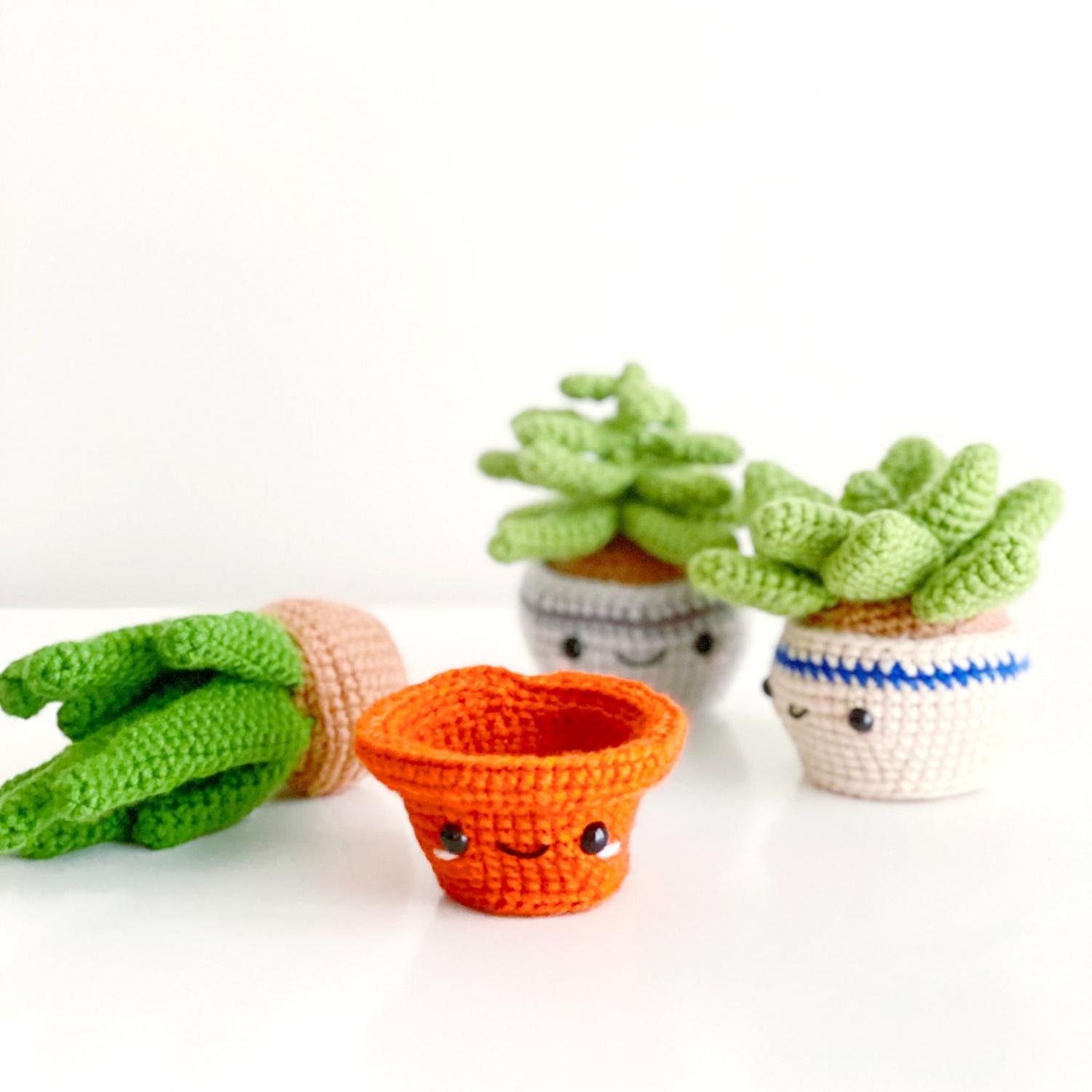 Some crochet House Plants succulents in orange, white, light blue, and light pink pots