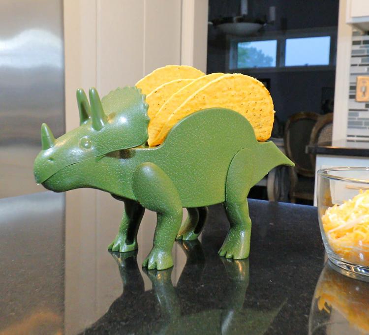 A green-colored dinosaur taco holder on a black kitchen top
