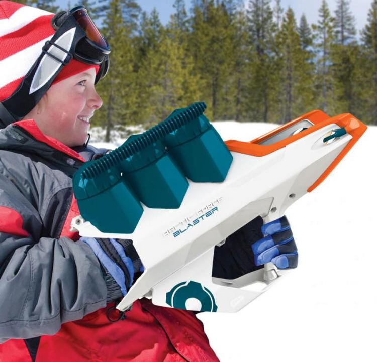 A boy wearing a red and grey jacket using a white, orange, and blue snowball blaster gun in the snow