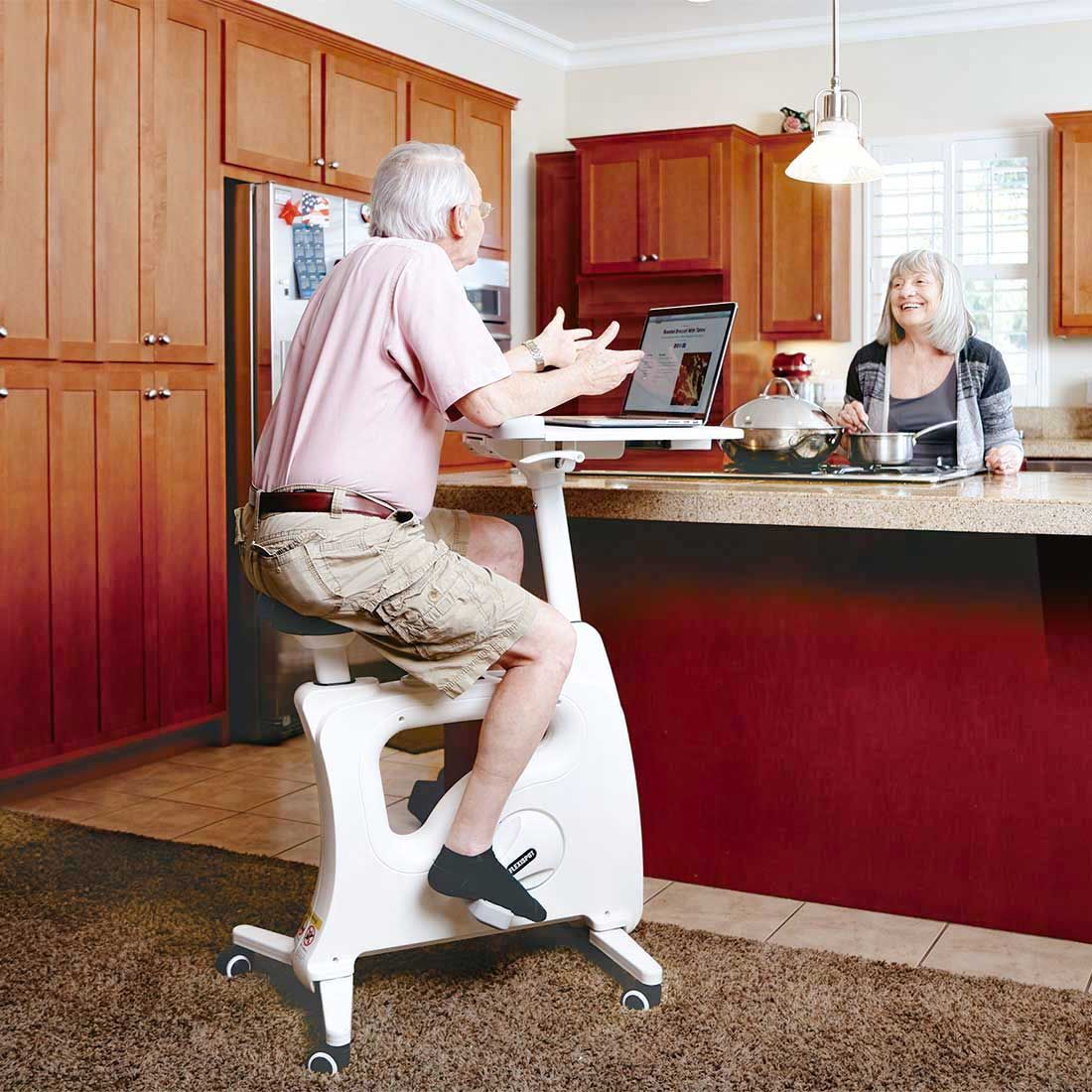 An old man wearing a pink shirt and khaki shorts sitting on a white Exercise Bike Desk