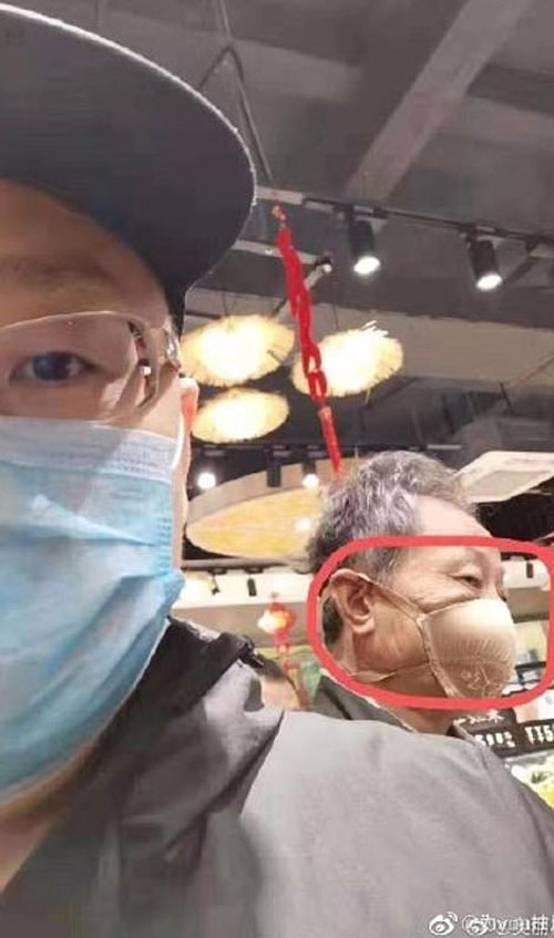 In a public place, a man got a selfie with an old man on his back wearing a bra as a mask