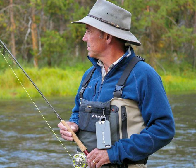A blue shirt wearing man holding fish rod in front of a lake