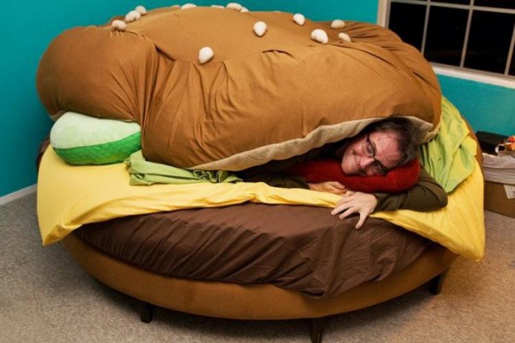 A man resting in a cheeseburger themed bed on a brown-skin rug
