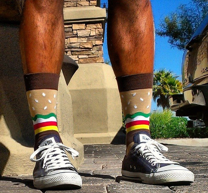 A man wearing cheeseburger socks with blue sneakers standing in the street
