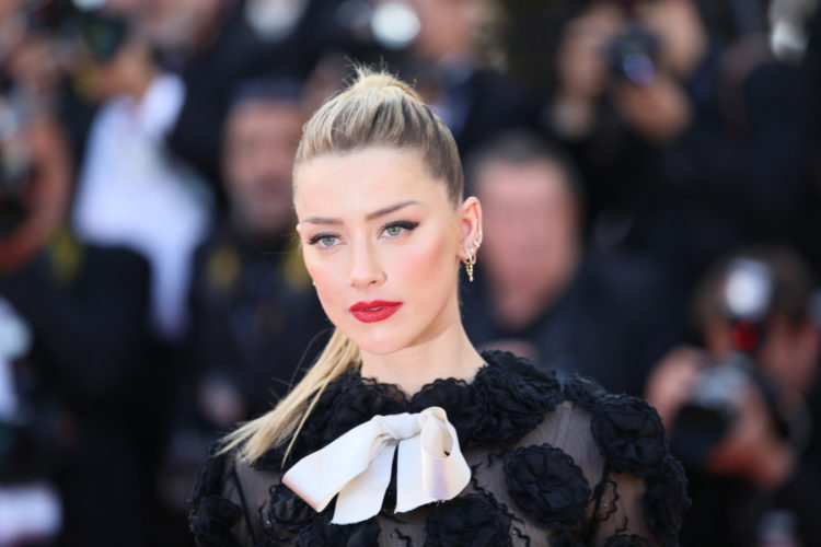 Amber Heard wearing a black lace dress with a big white bow with papparazi behind her