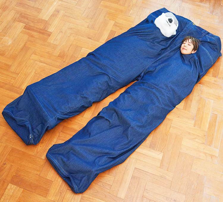A girl and a toy sleeping in a blue colored giant pants bed on the wooden floor