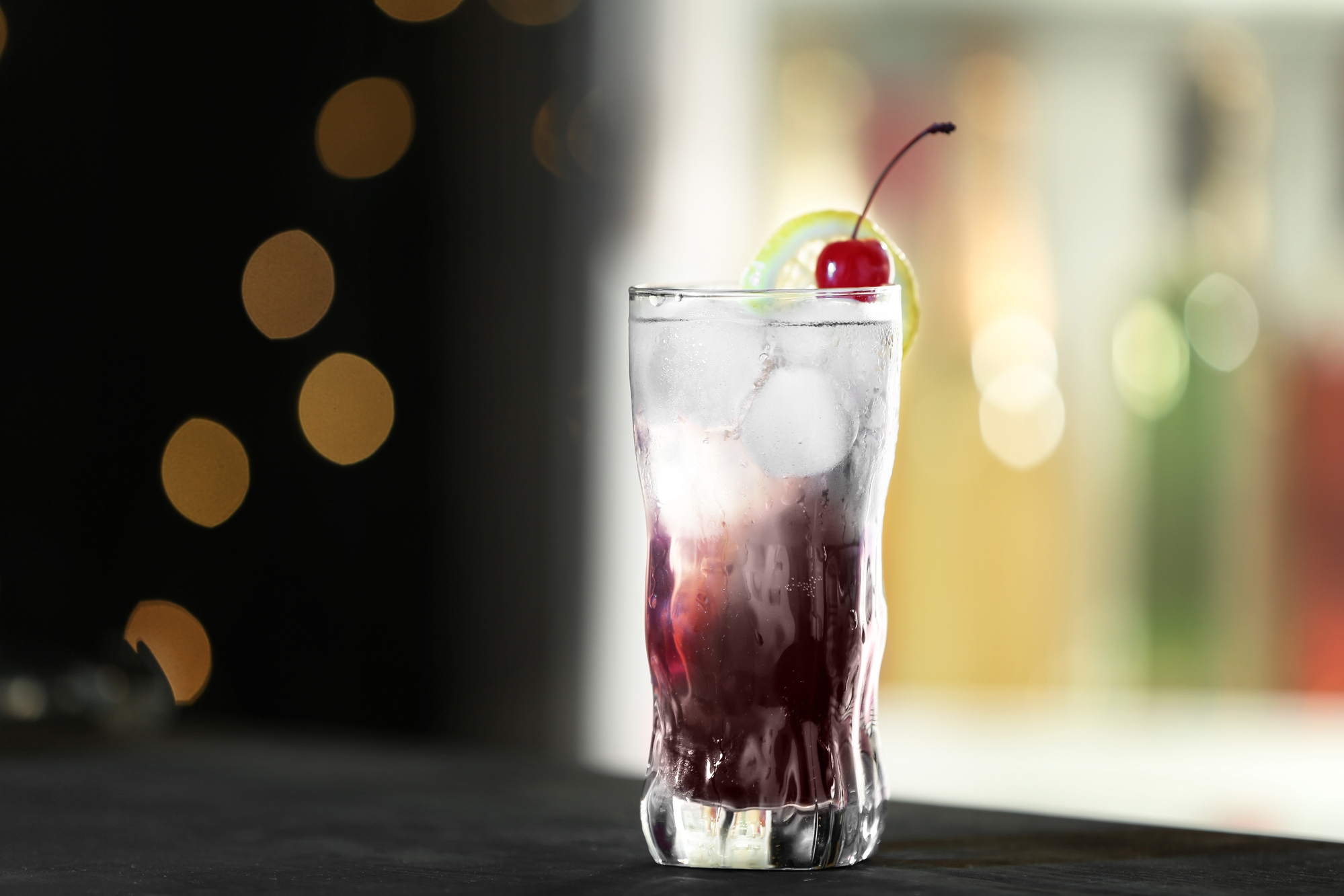 Black superman drink in a glass decorated with cherry placed on a black surface