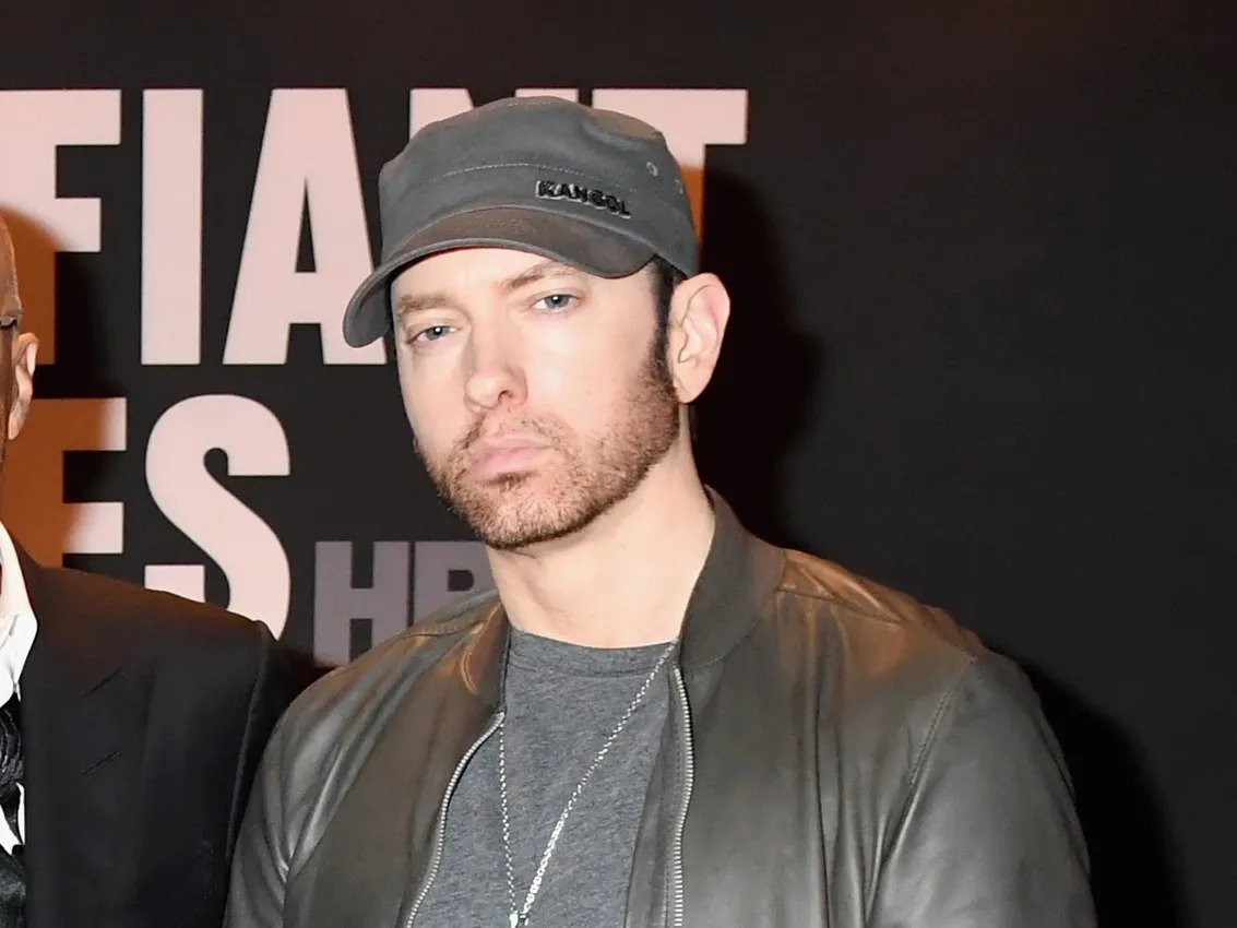 Eminem in his beard look wearing a black jacket and a black cap