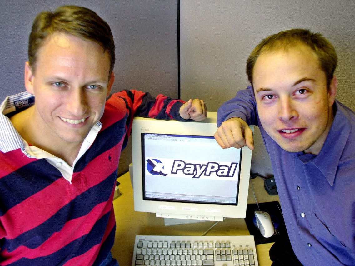 Peter Theil on the left and Elon Musk on the right are both smiling at the camera, with an old computer in the middle