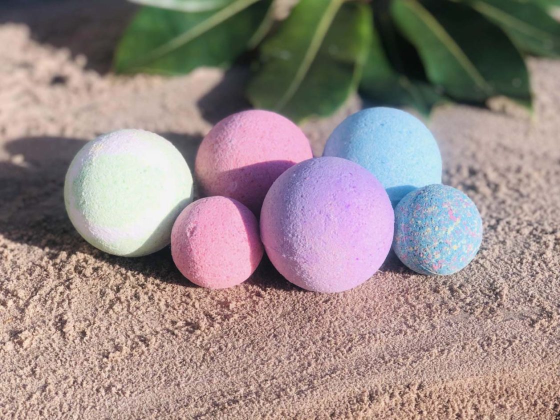 Pink, purple, blue and green bath bombs placed on sand