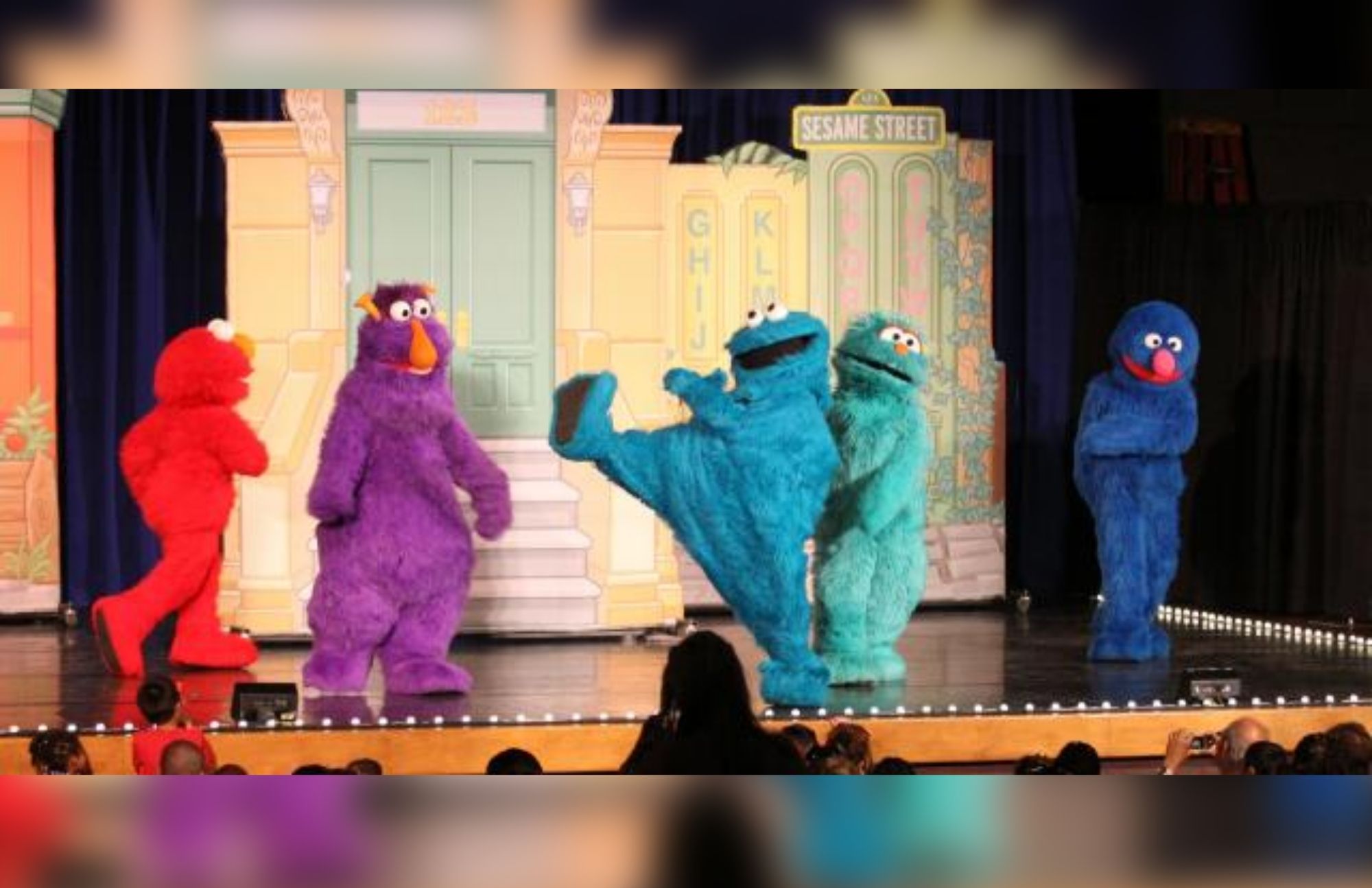 Five muppets with different colors are performing in the stage in front of many people
