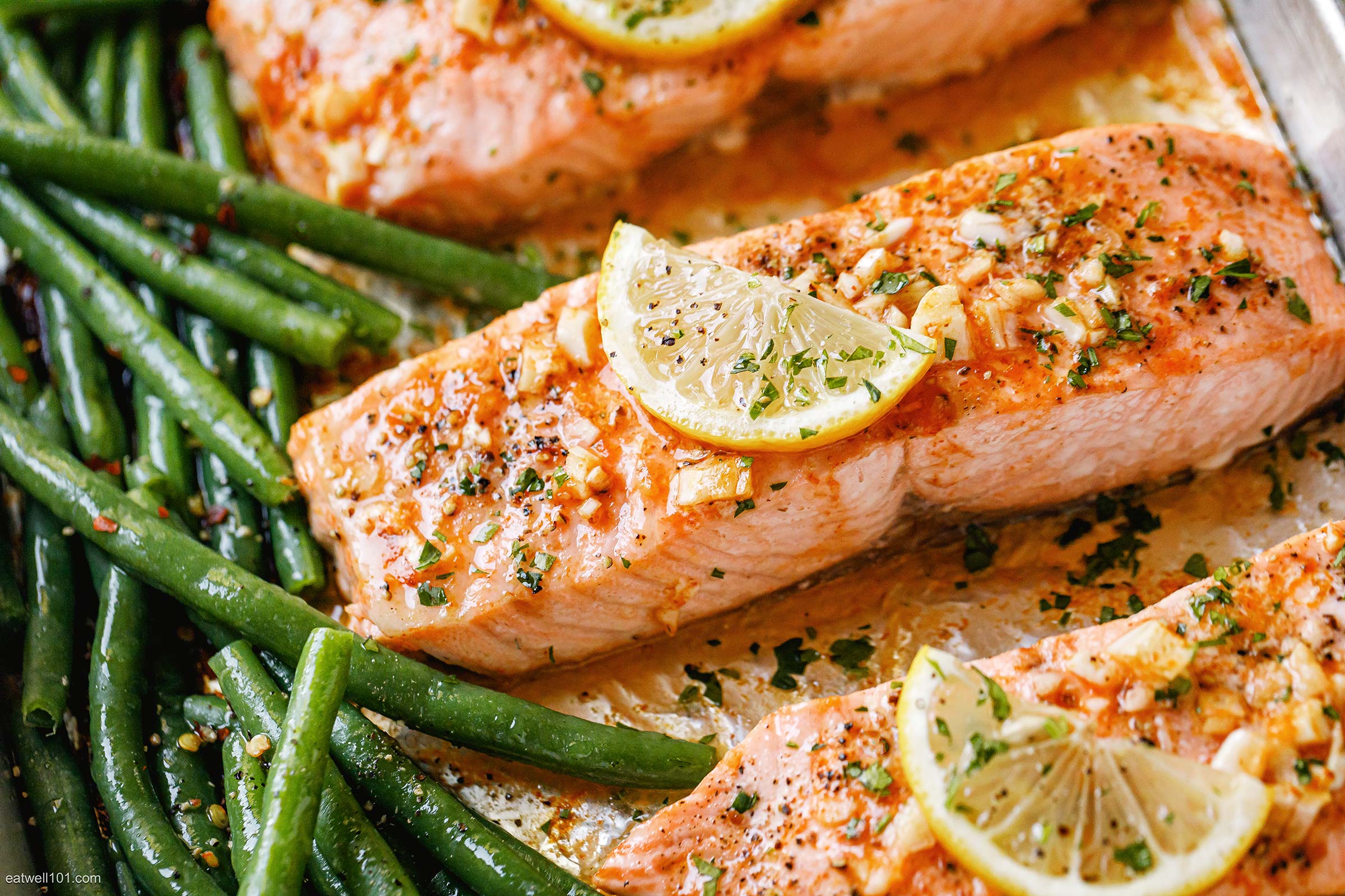 Cooked salmon fish meat topped with sliced lemons and string beans as garnish